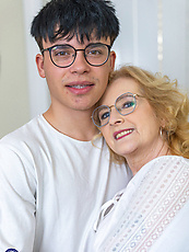Mature woman in leather skirt and stockings embraces young man on sofa